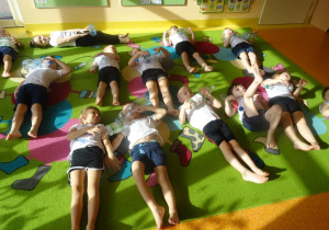 Dzieci leżą na plecach, butelki plastikowe turlają po brzuchu.